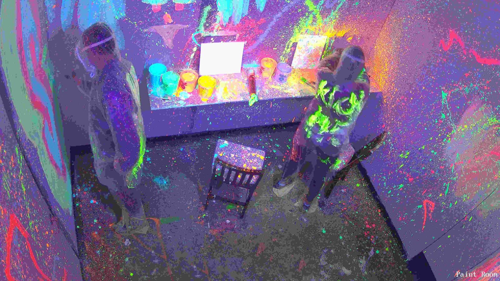 Two guests throwing glowing paint in a UV paint splatter room
