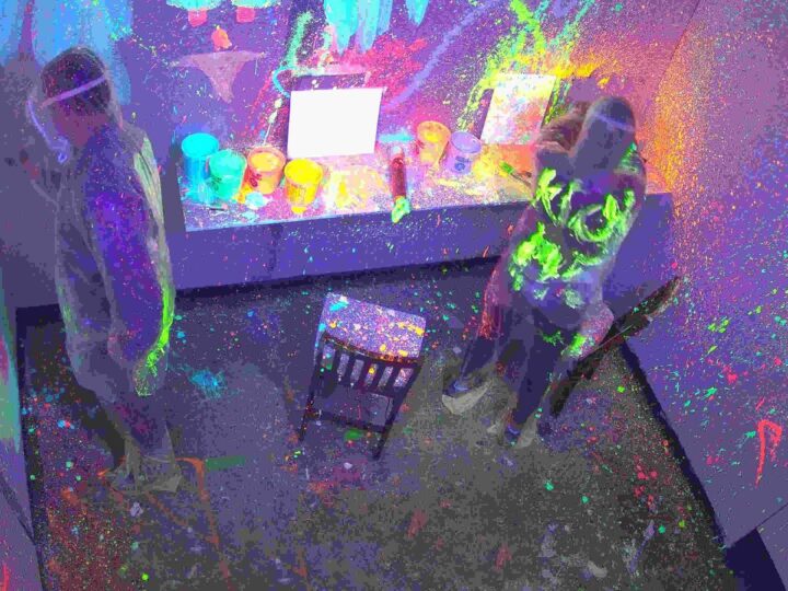 Two guests throwing neon paint in the UV paint splatter room