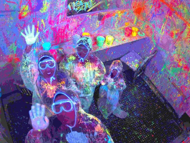 Family in white suits covered in glowing UV paint, waving at the camera